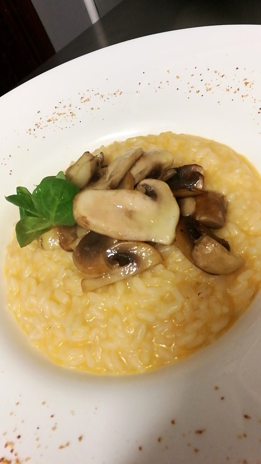 Risotto cremoso ai funghi su un piatto bianco, guarnito con funghi e prezzemolo.
