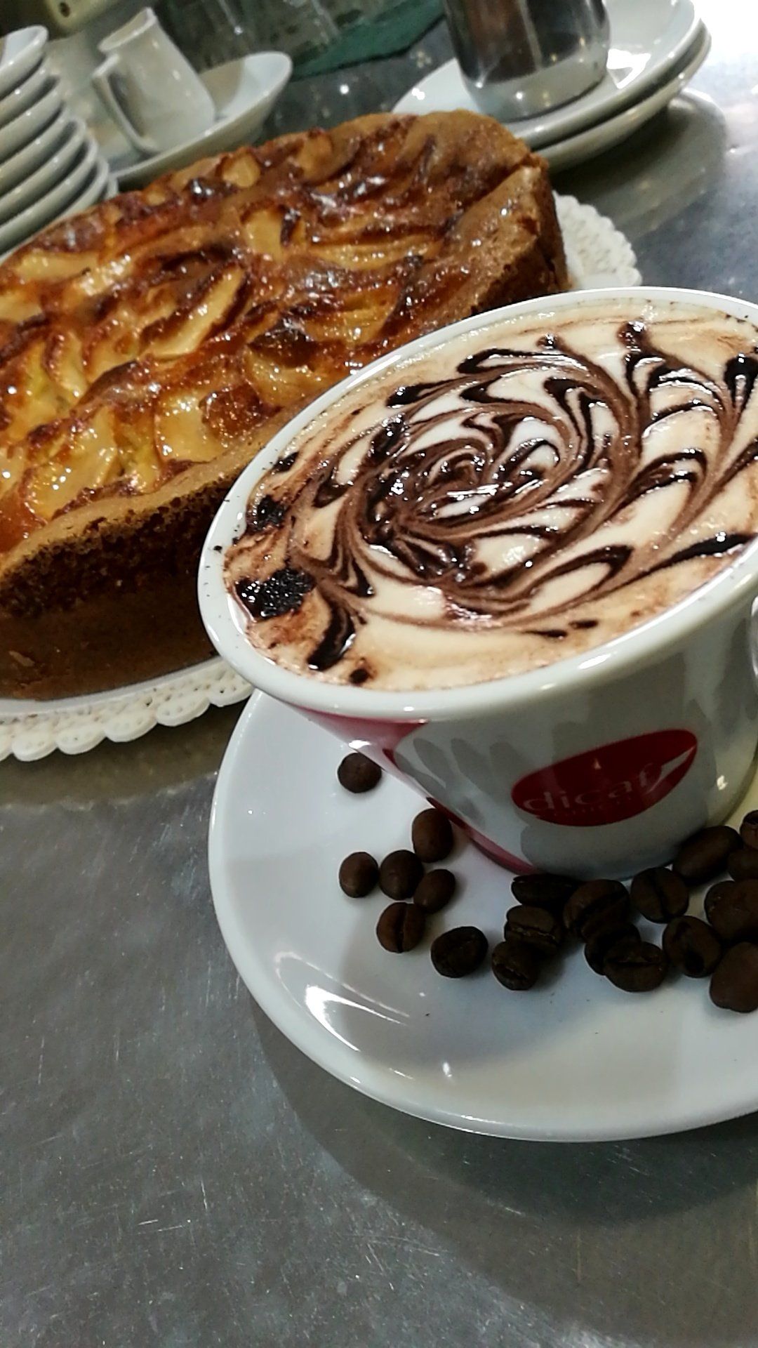 Cappuccino con cioccolato, chicchi di caffè e torta di mele su una superficie metallica.