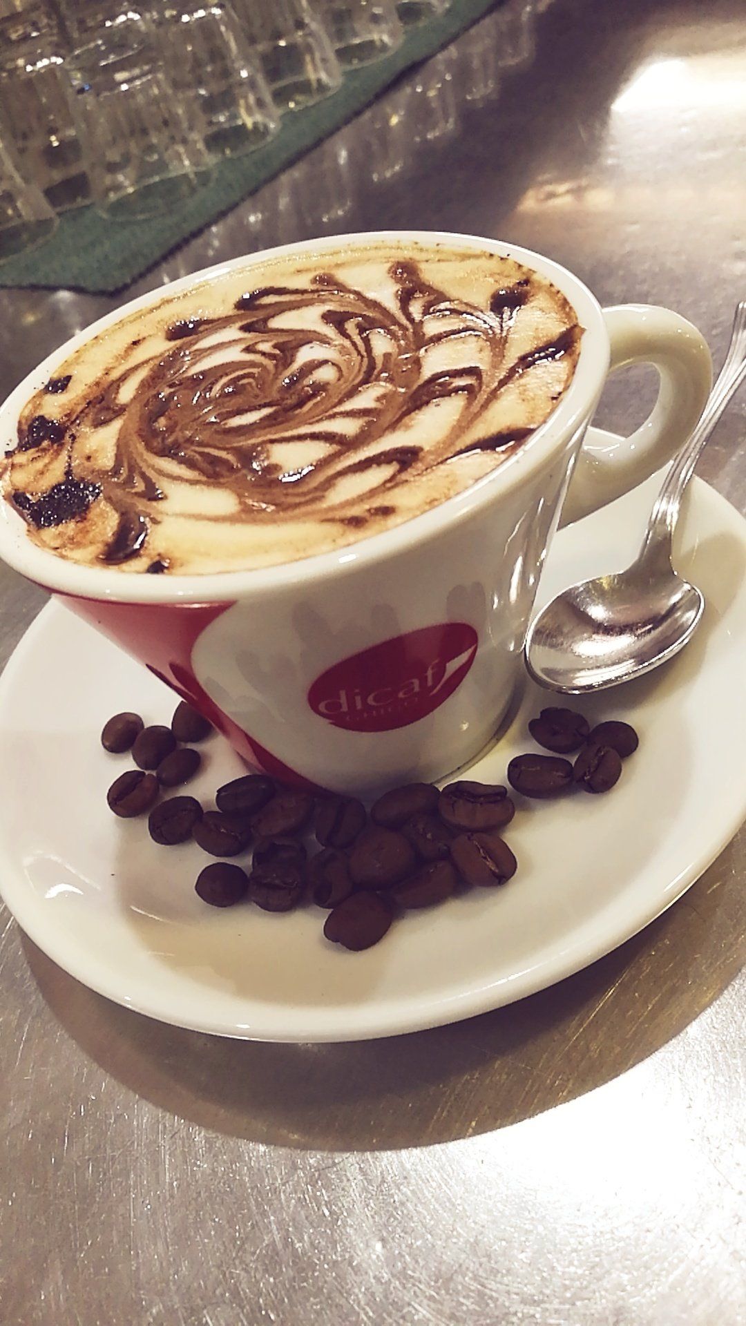 Cappuccino in una tazza, con cioccolato, su un piattino con chicchi di caffè e un cucchiaino.