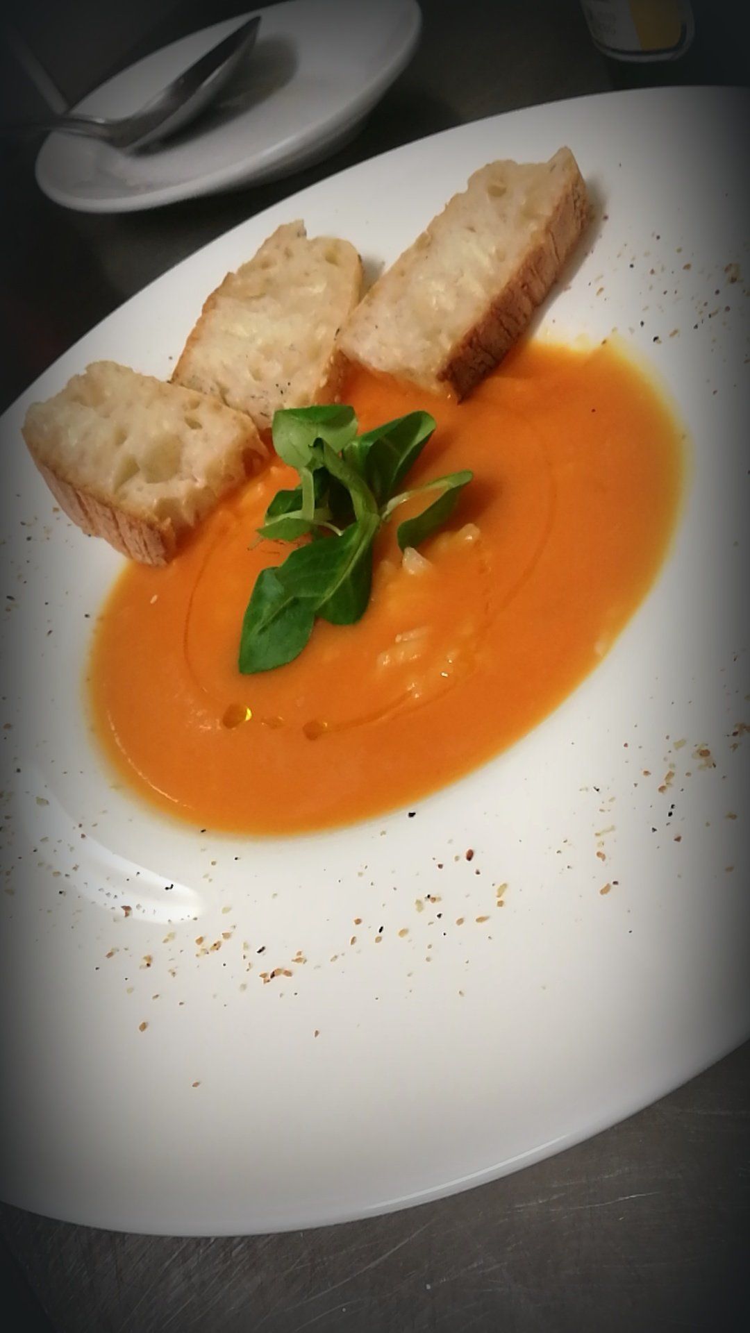 Zuppa d'arancia in una ciotola ovale bianca, guarnita con verdure e servita con pane.