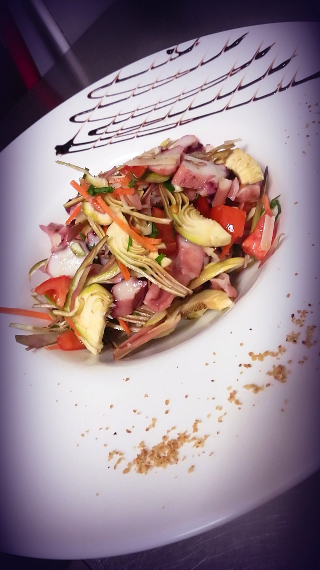 Insalata con carciofi, pomodori e prosciutto, condita con glassa balsamica, servita su un piatto bianco.