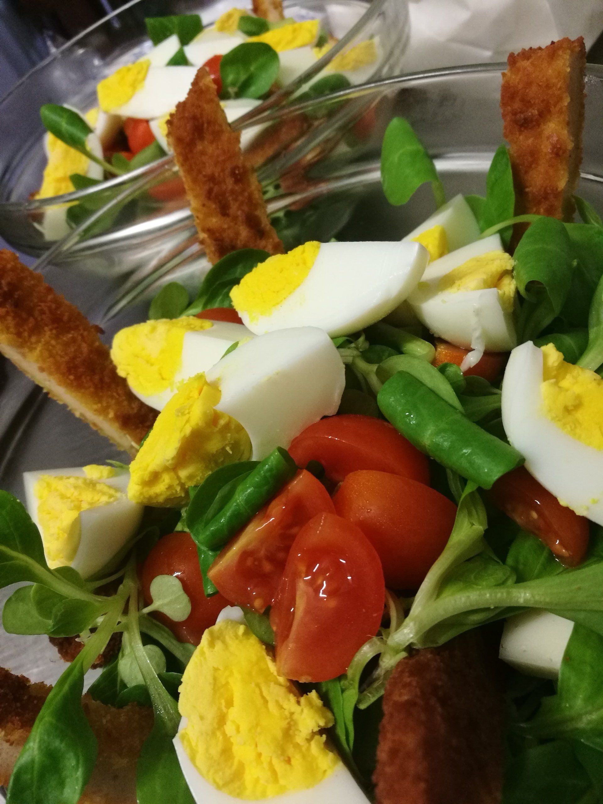 Insalata con uova sode, pomodori, crostini di pane e foglie verdi in ciotole di vetro.