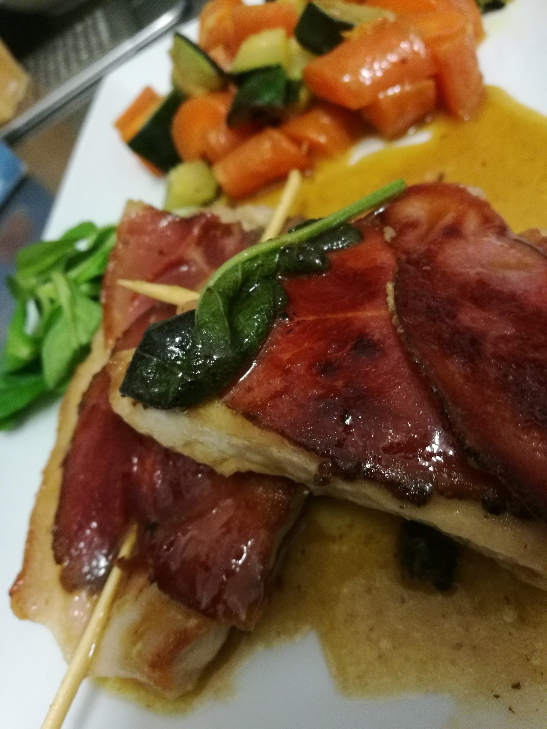 Pollo avvolto nel prosciutto, servito con verdure e salsa.