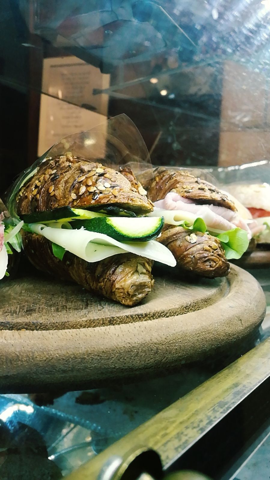 Panini su un vassoio di legno in una vetrina. Croissant integrali ripieni di formaggio, cetriolo e verdure.