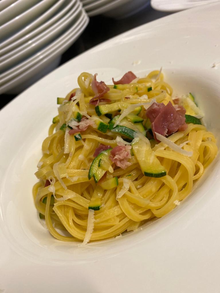 Pasta con zucchine, prosciutto e parmigiano su un piatto bianco.