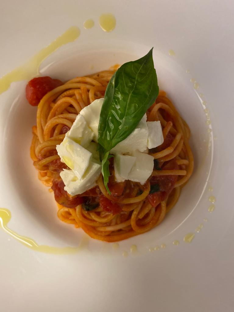 Spaghetti con salsa di pomodoro, mozzarella, basilico e un filo d'olio su un piatto bianco.