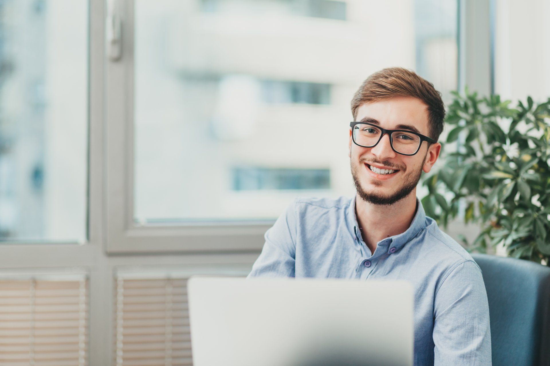 A man is sitting in front of a laptop computer and smiling.