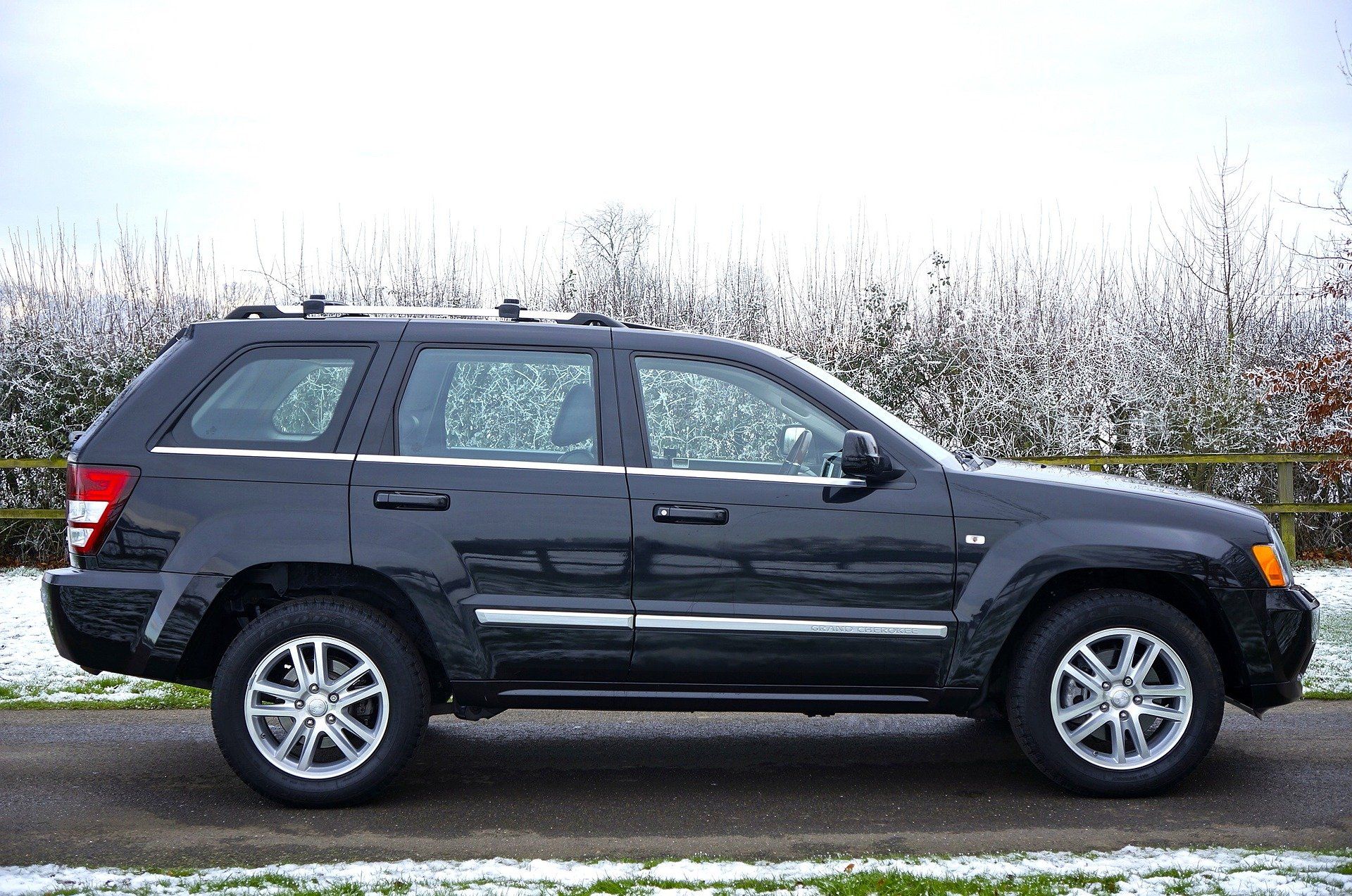 Black Jeep Grand Cherokee SUV parked on a road with a snowy backdrop.