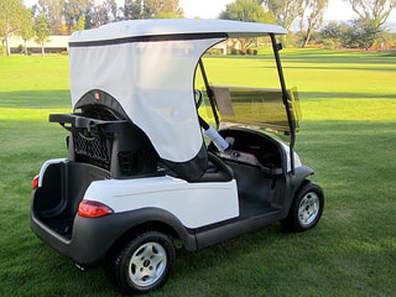 A white golf cart with a canopy is parked on a lush green golf course.