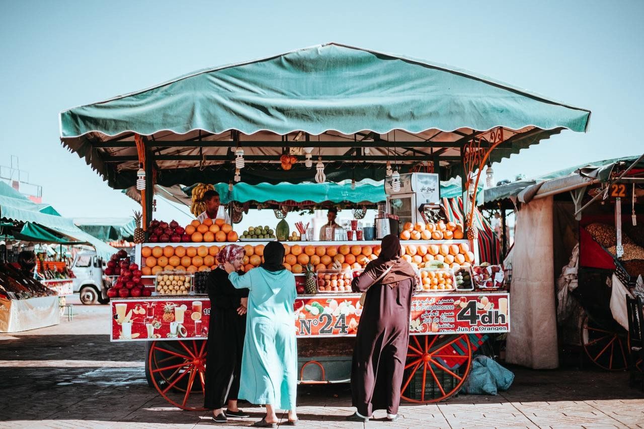 A group of people are standing in front of a fruit stand.