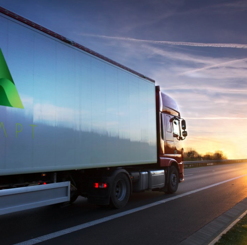 A semi truck is driving down a highway at sunset.