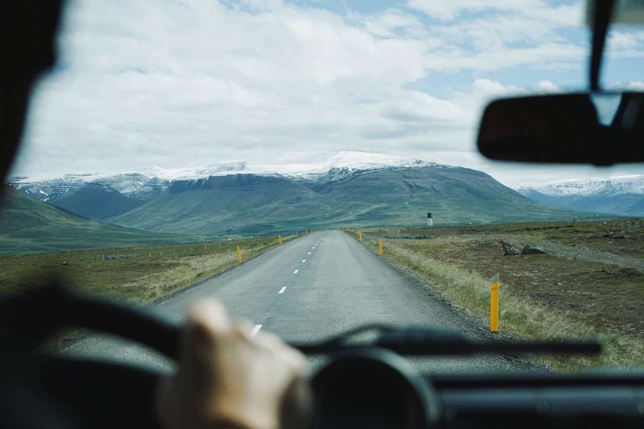 A person is driving down a road with mountains in the background.