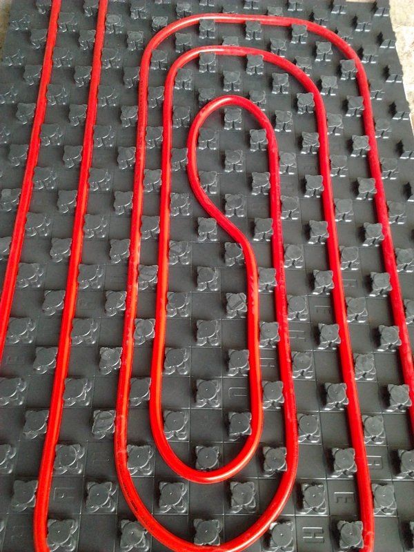 Tubi di riscaldamento rossi installati a spirale su un pannello isolante per riscaldamento a pavimento nero con borchie.