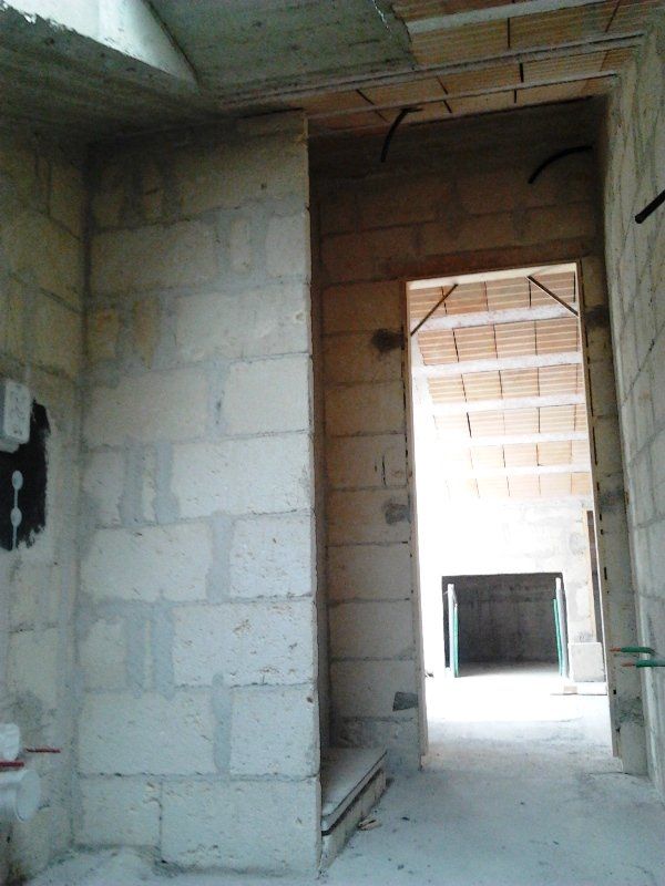 Una stanza interna in costruzione, ancora da rifinire, con pareti in blocchi di muratura di colore chiaro, una porta e un soffitto piastrellato.