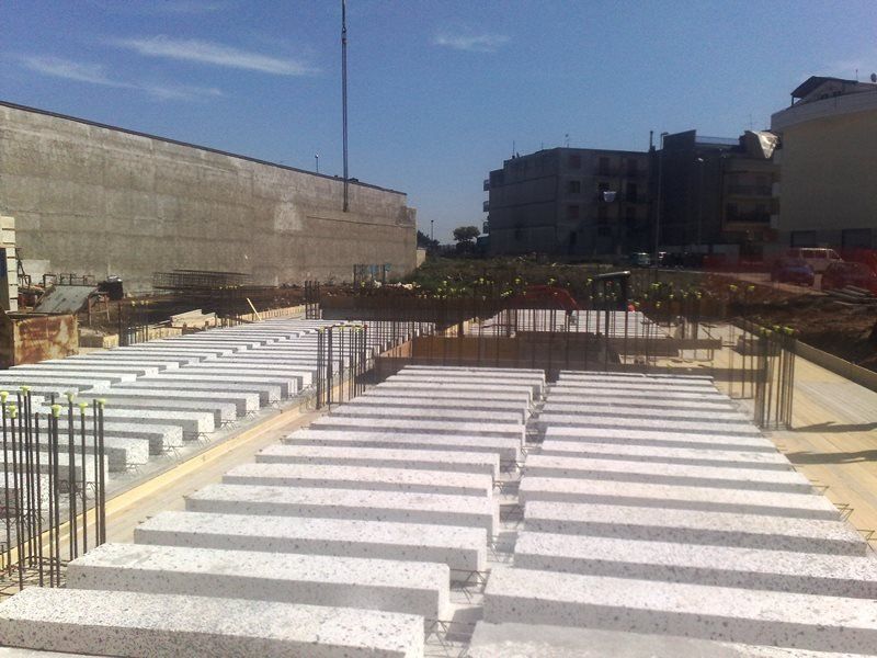 File di blocchi di cemento bianchi e rettangolari disposti in un cantiere, con edifici sullo sfondo.