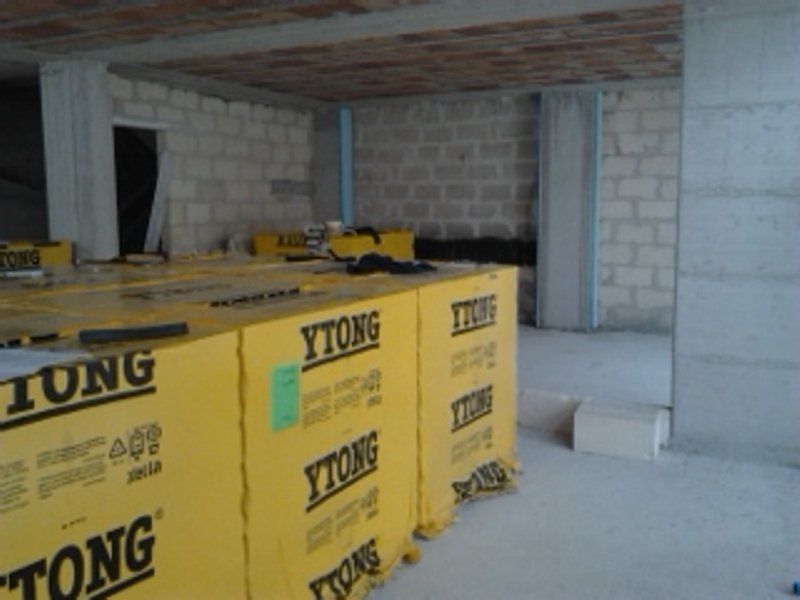 Pile di blocchi da costruzione Ytong avvolti in carta gialla, accatastati su un pavimento di cemento all'interno di un edificio incompiuto.