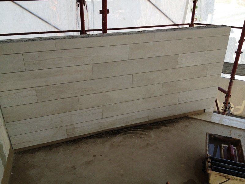 In un cantiere edile con impalcature, una parete parzialmente rivestita con piastrelle orizzontali color beige chiaro effetto legno.