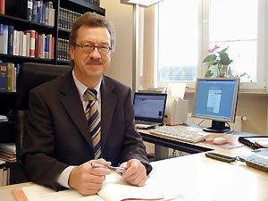Ein Mann in Anzug und Krawatte sitzt an einem Schreibtisch vor einem Computer.