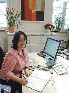 Eine Frau in einem rosa Hemd sitzt an einem Schreibtisch mit einem Computer.