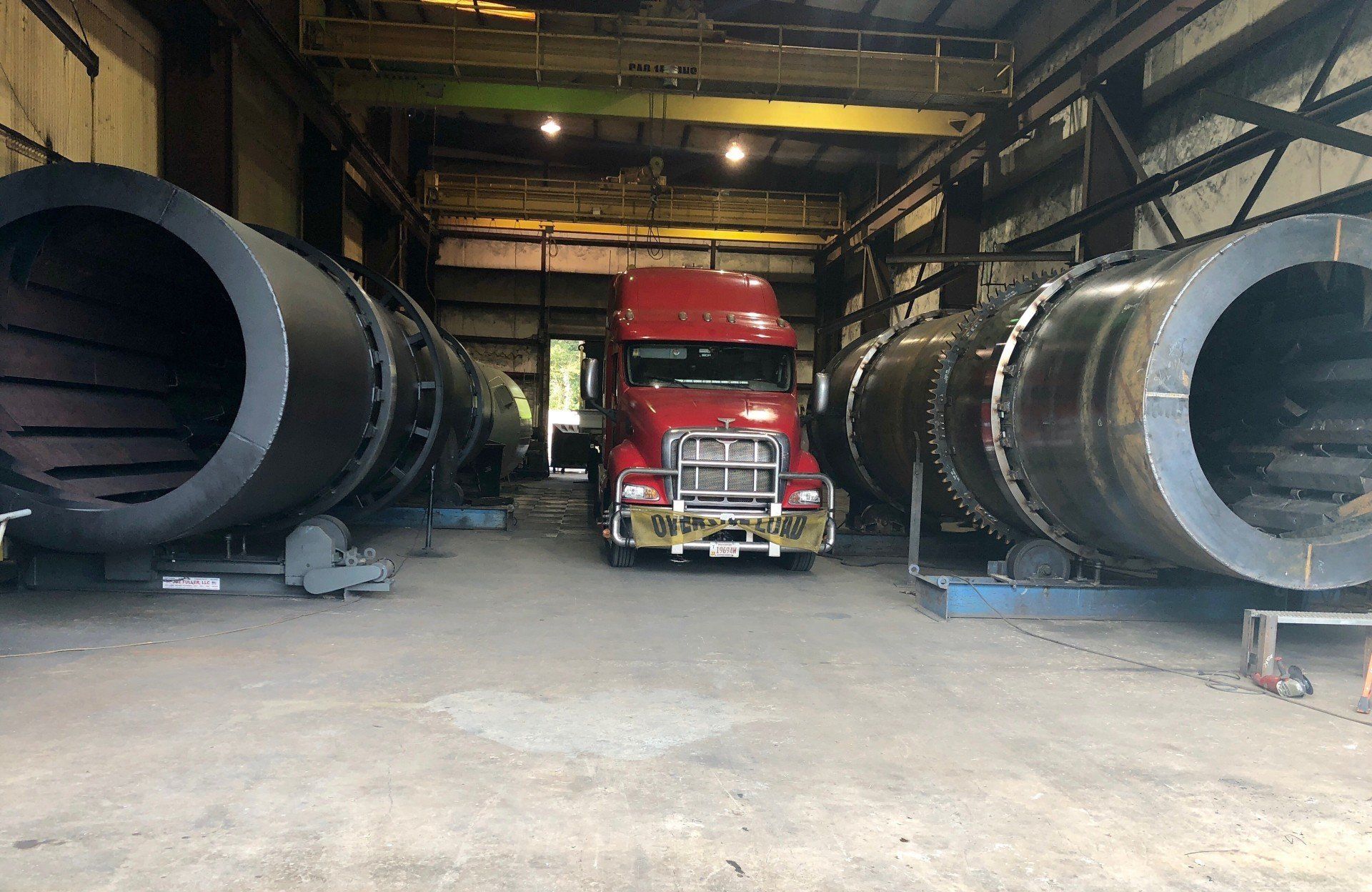 A red semi truck is parked in a warehouse filled with large pipes.