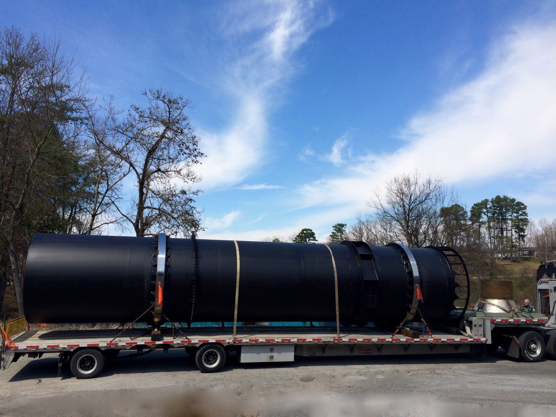A large black pipe is being transported on a flatbed truck