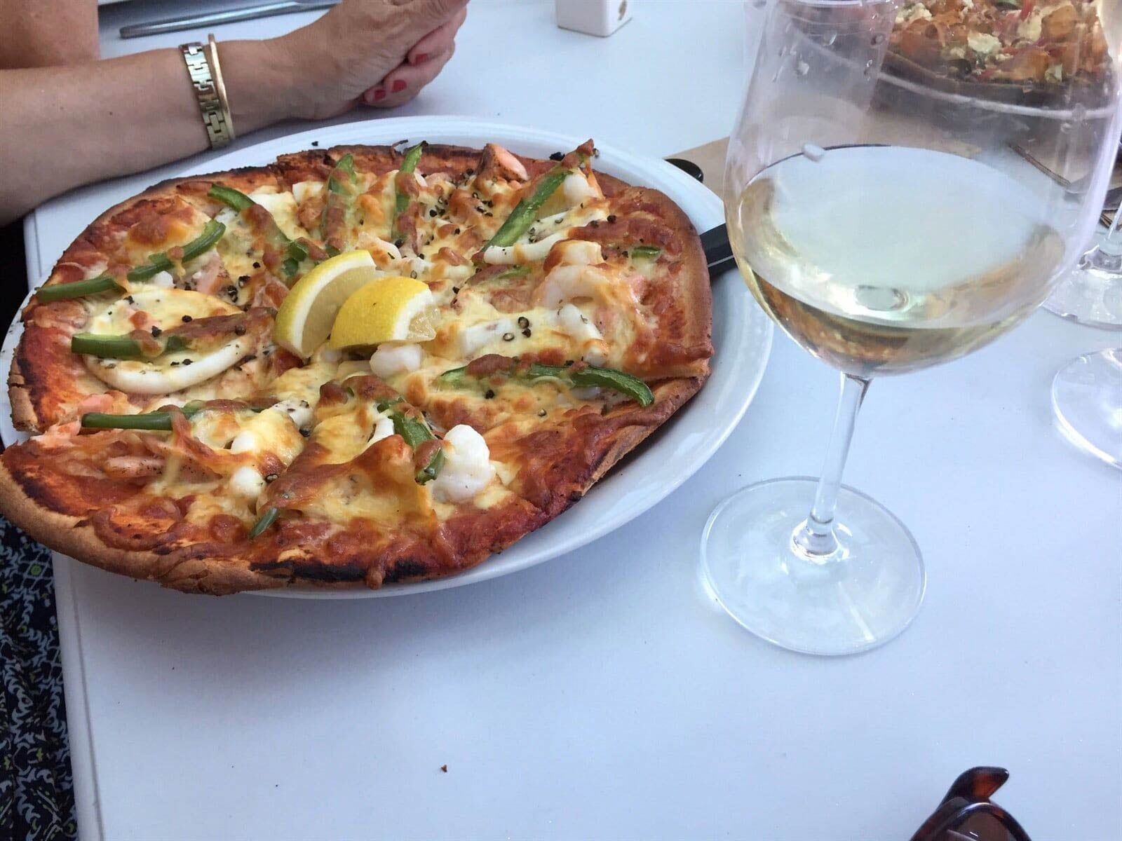 Seafood flatbread pizza with lemon wedge and glass of white wine on a white table — Café & Bottle Shop Fingal Bay, QLD