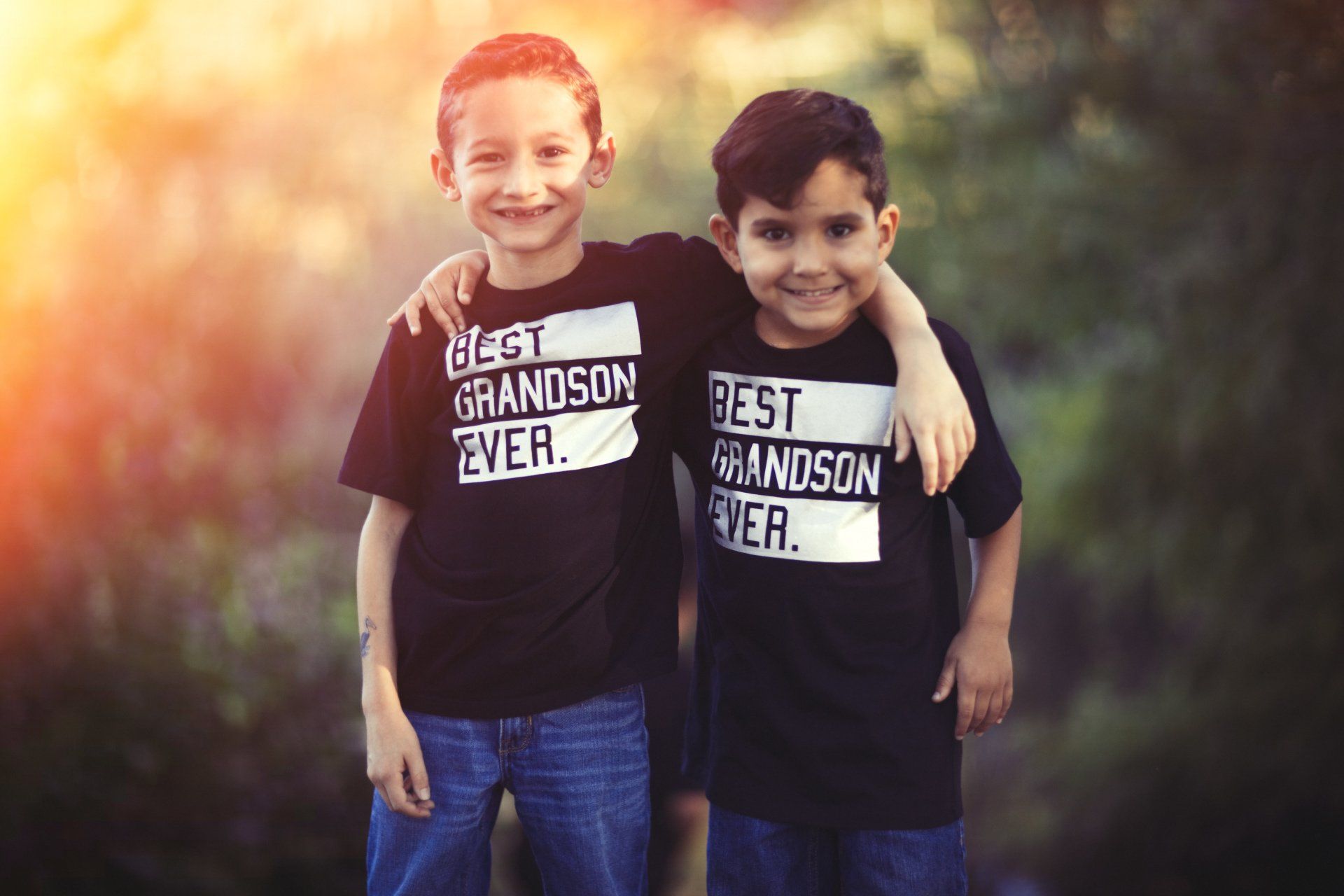 Two young boys wearing black shirts that say `` best grandson ever '' are standing next to each other.