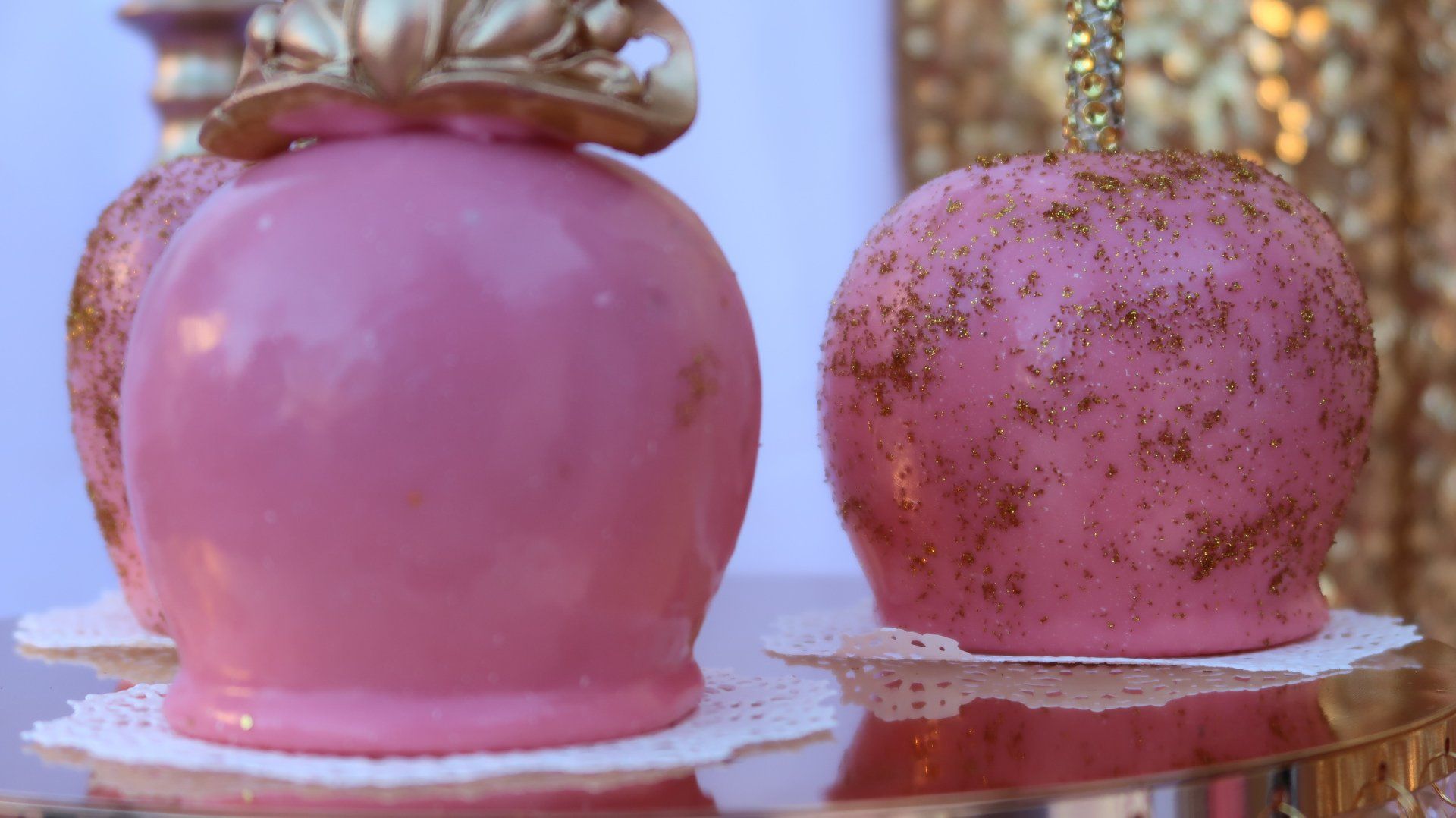Two pink candy apples with gold sprinkles are sitting on a table.