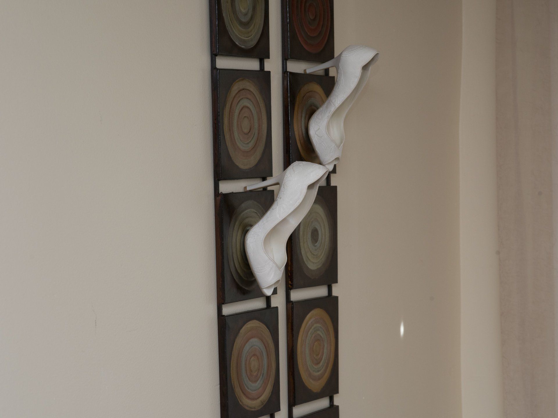 A pair of white high heels are hanging on a wall.