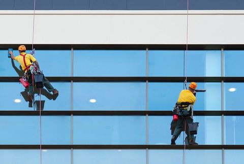 Two window washers suspended by ropes, cleaning windows on a modern building.