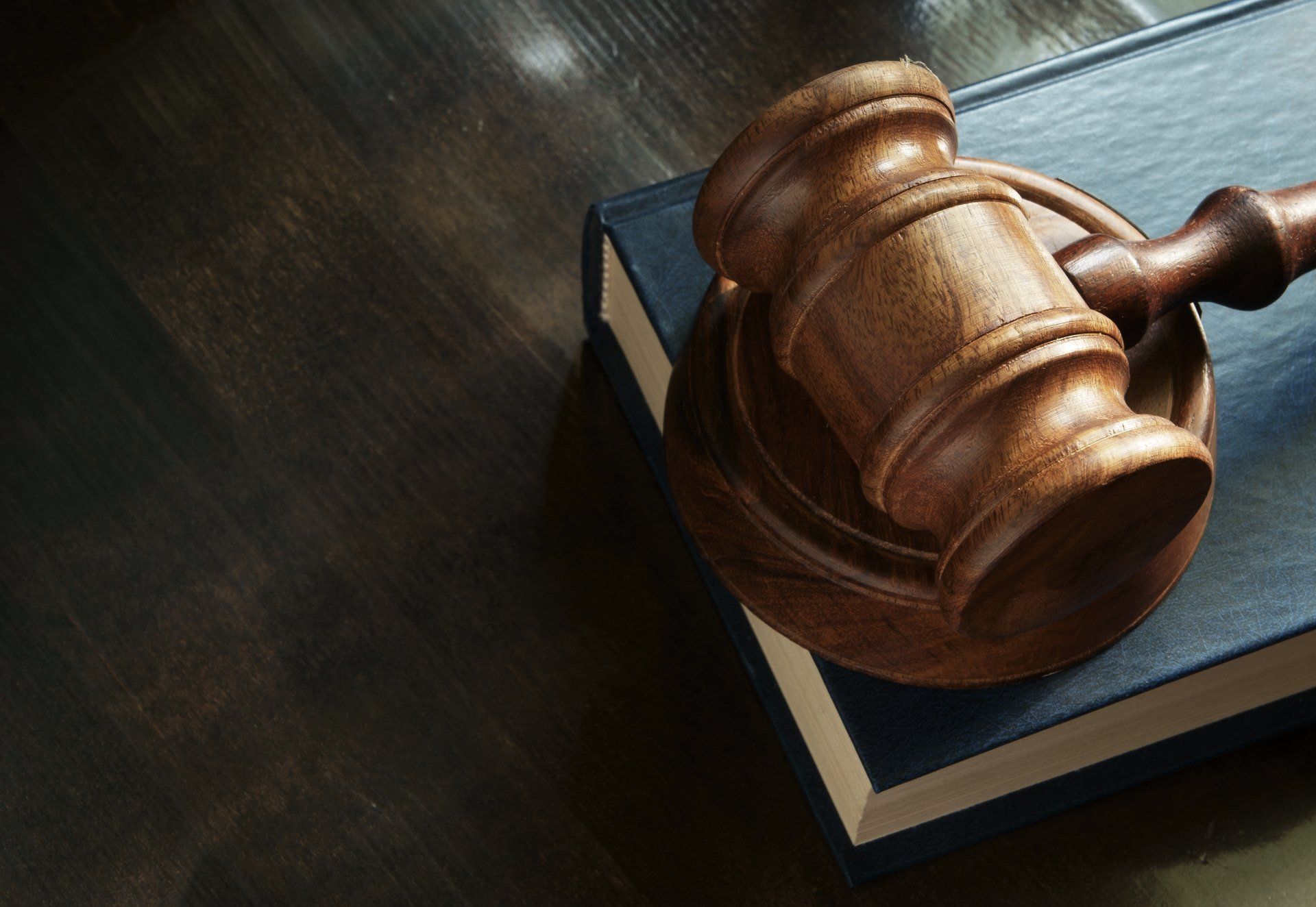 Martelletto di legno posto sopra un libro chiuso con copertina blu, su una superficie di legno scuro.