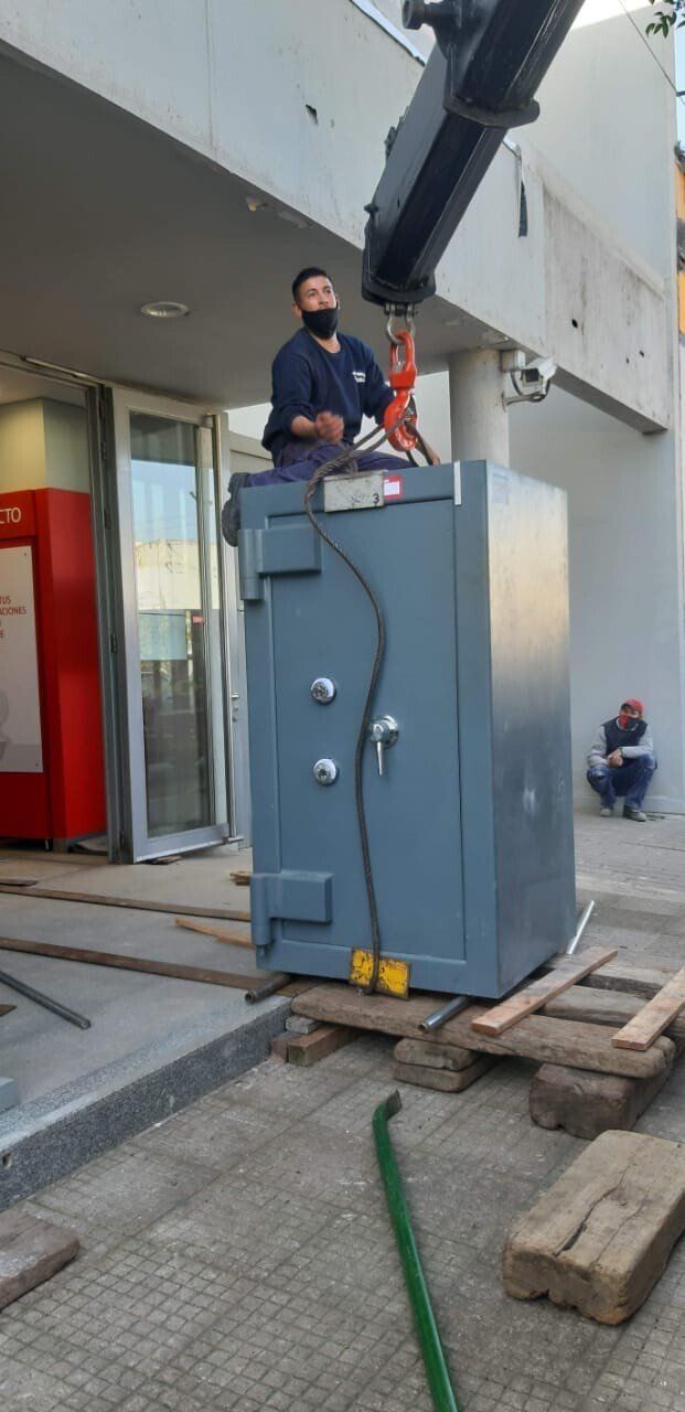 Un hombre está de pie encima de una caja fuerte que está siendo levantada por una grúa.
