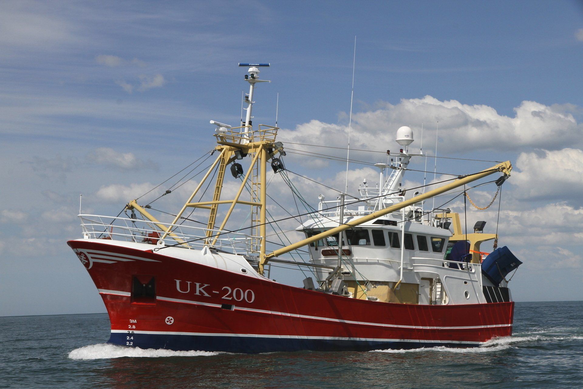 Der rot-weiße Fischkutter „UK-209“ kreuzt auf dem Wasser unter blauem Himmel.