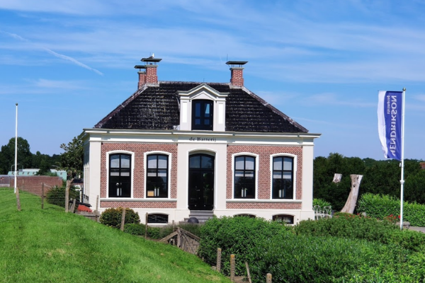Holländisches Haus mit Backsteinverkleidung und schwarzen Fenstern, grüner Hügel davor, blauer Himmel.