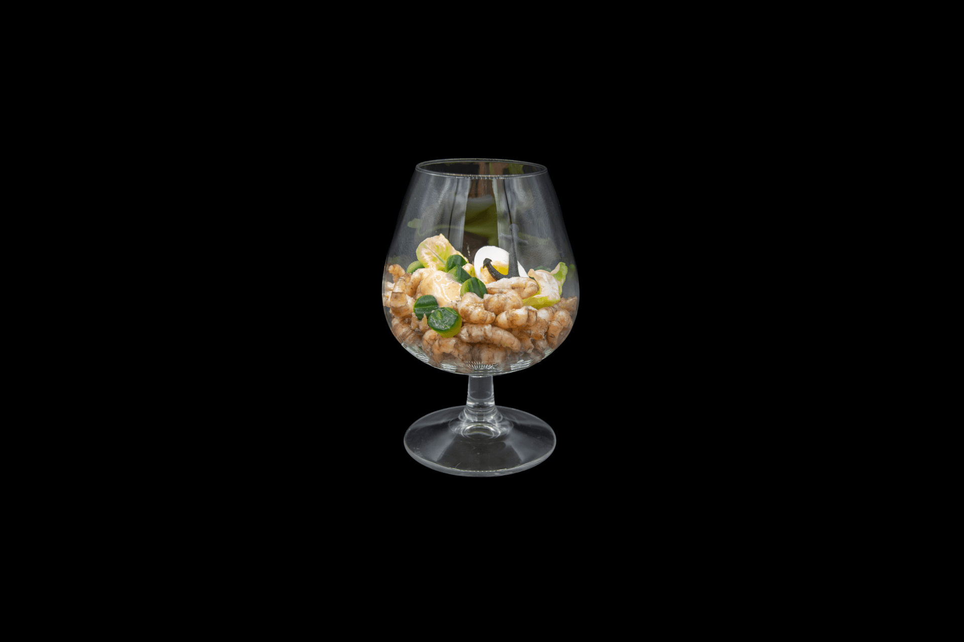 Ein Glas mit Lebensmitteln, darunter Nüsse und Früchte, vor schwarzem Hintergrund.