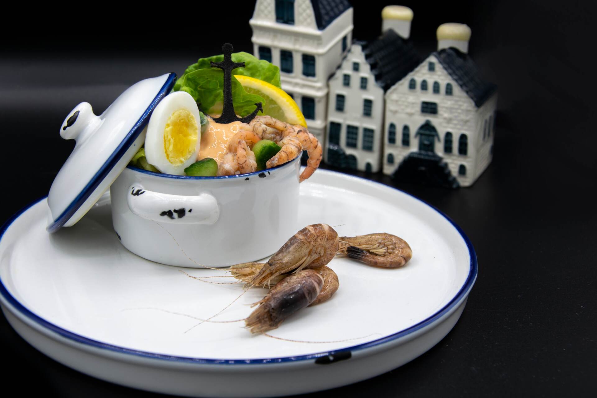 Garnelen- und Eiersalat in einer weißen Schüssel, Garnelen auf einem Teller, Miniaturhäuser im Hintergrund.