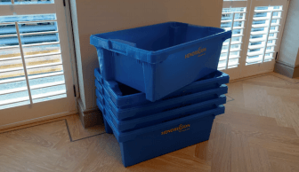 Blue storage bins stacked on a hardwood floor, near closed shutters.
