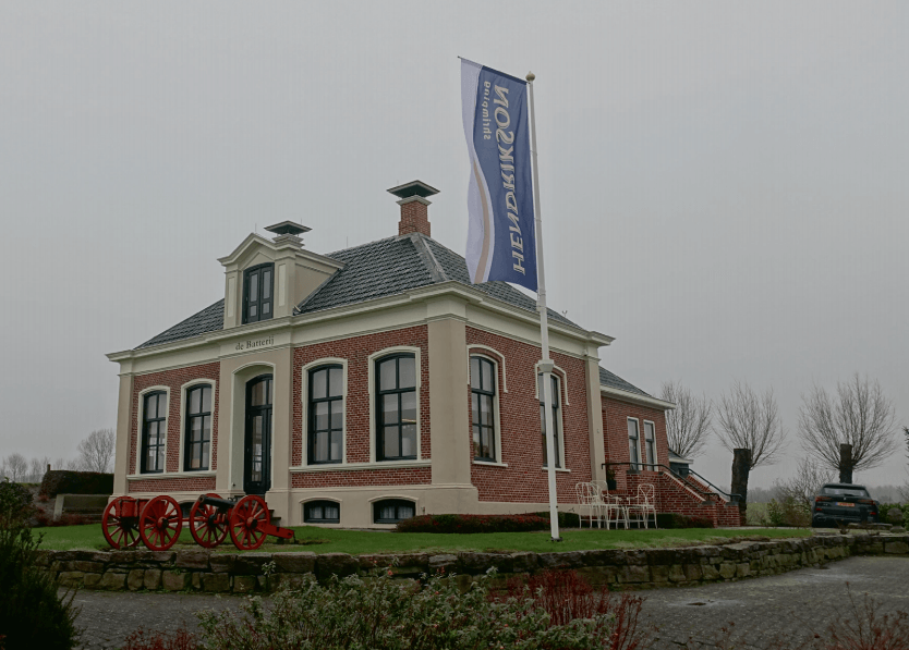 Brick building with flag on overcast day, red cannons in front.