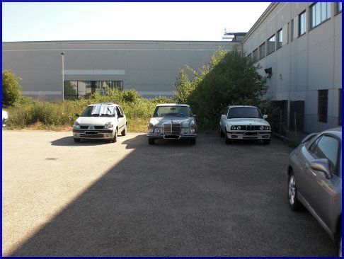 Drei Autos stehen auf einem Parkplatz vor einem Gebäude