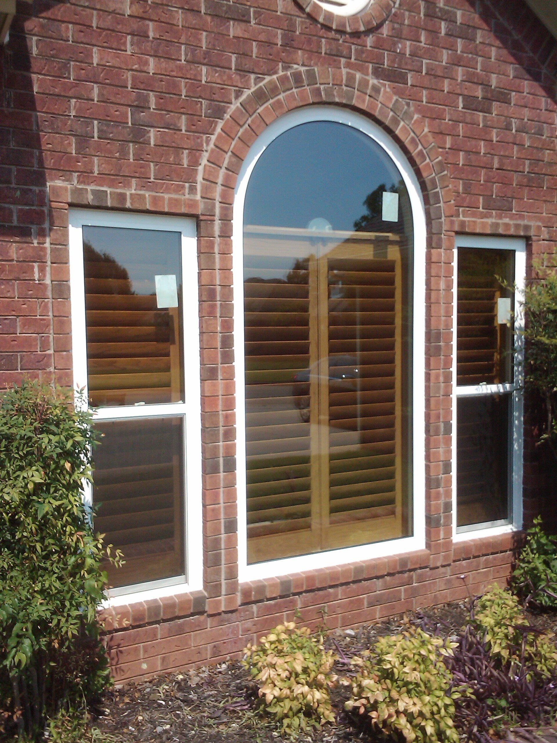 Brick wall with arched and rectangular windows; light-colored shutters visible.
