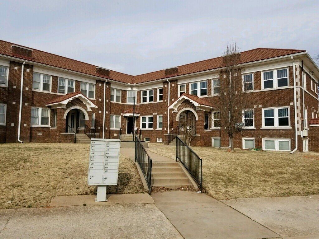 Apartment building with brick exterior, brown roof, and mailbox in front.