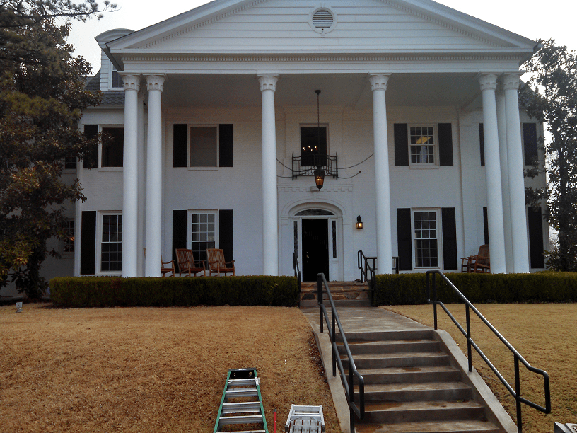 White house with large columns and black shutters; steps lead up to the open front door.
