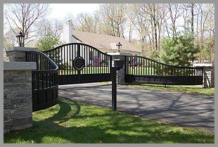 A large black gate is open to a driveway leading to a house.