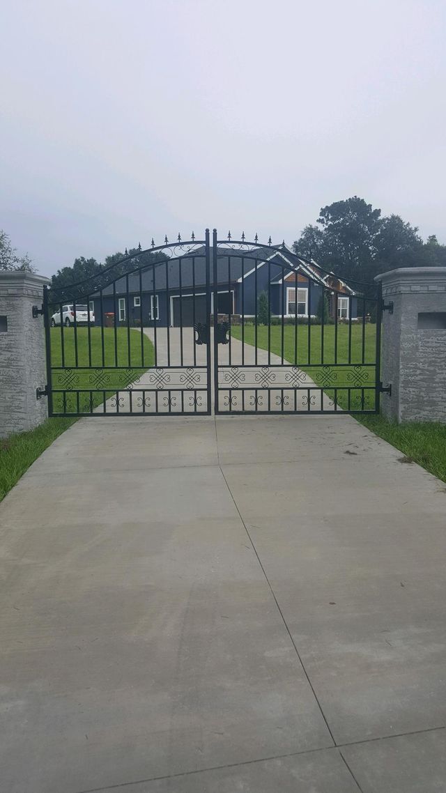 A black gate is open to a driveway leading to a house.