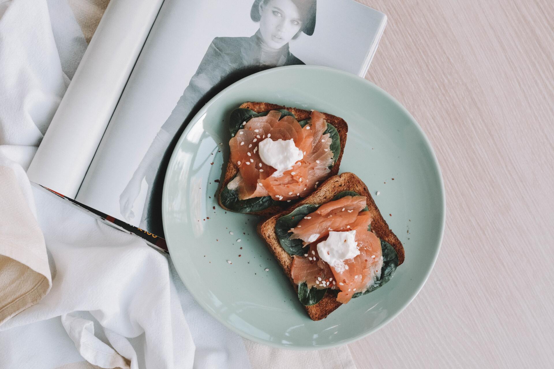 ROM&ROM  Dos rebanadas de pan tostado con mantequilla y azúcar glas sobre un plato verde pálido junto a una revista abierta.