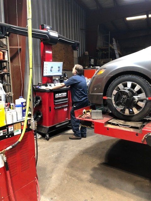 Mechanic adjusting car alignment using equipment in a garage. A car is on a lift.