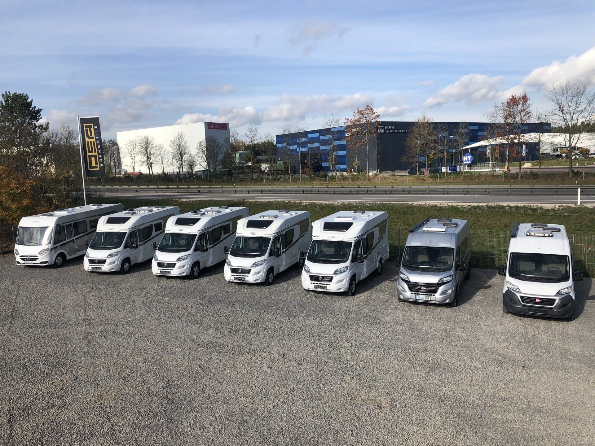 A row of rvs are parked in a gravel lot.