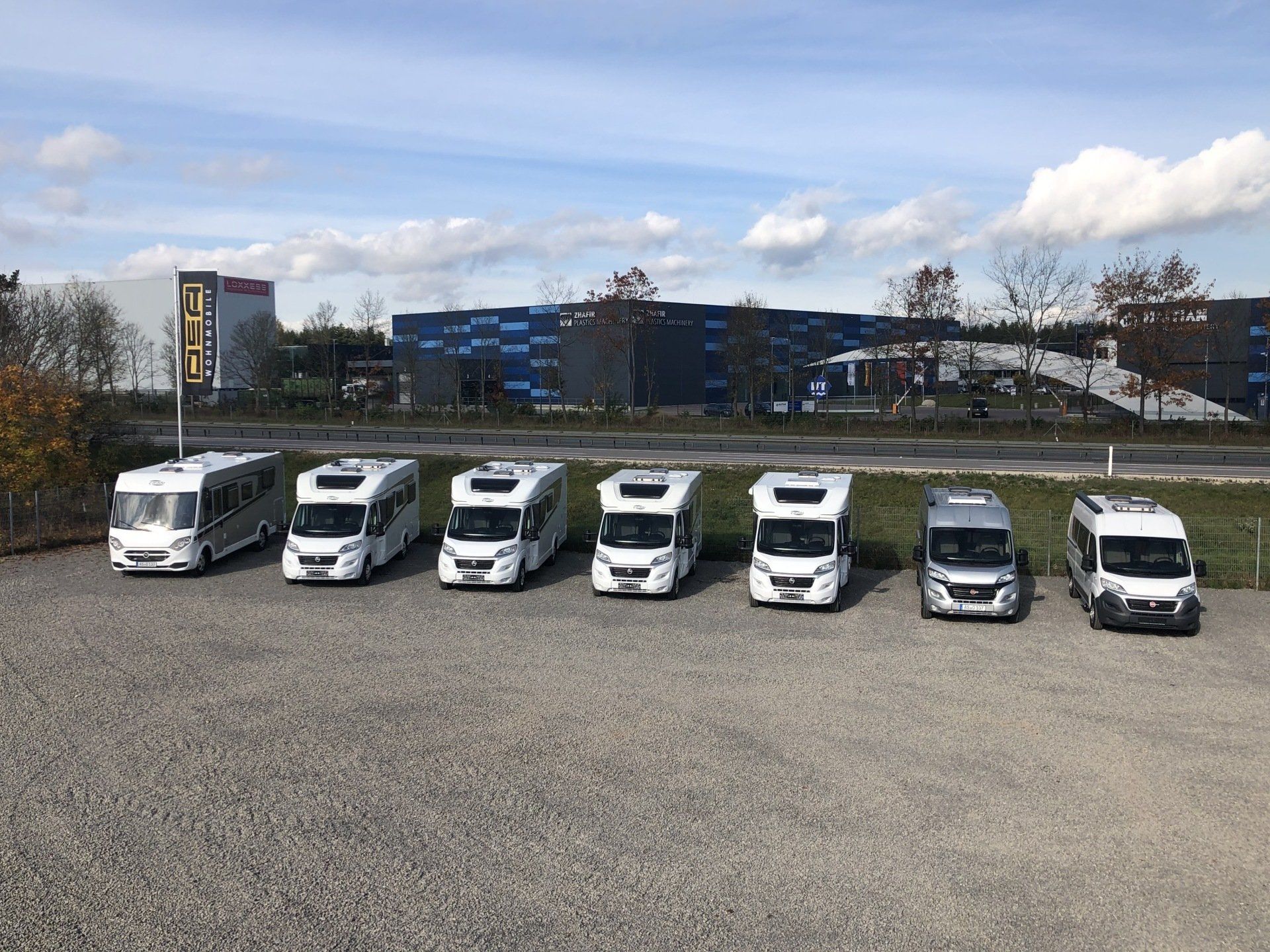 A row of camper vans are parked in a gravel lot.