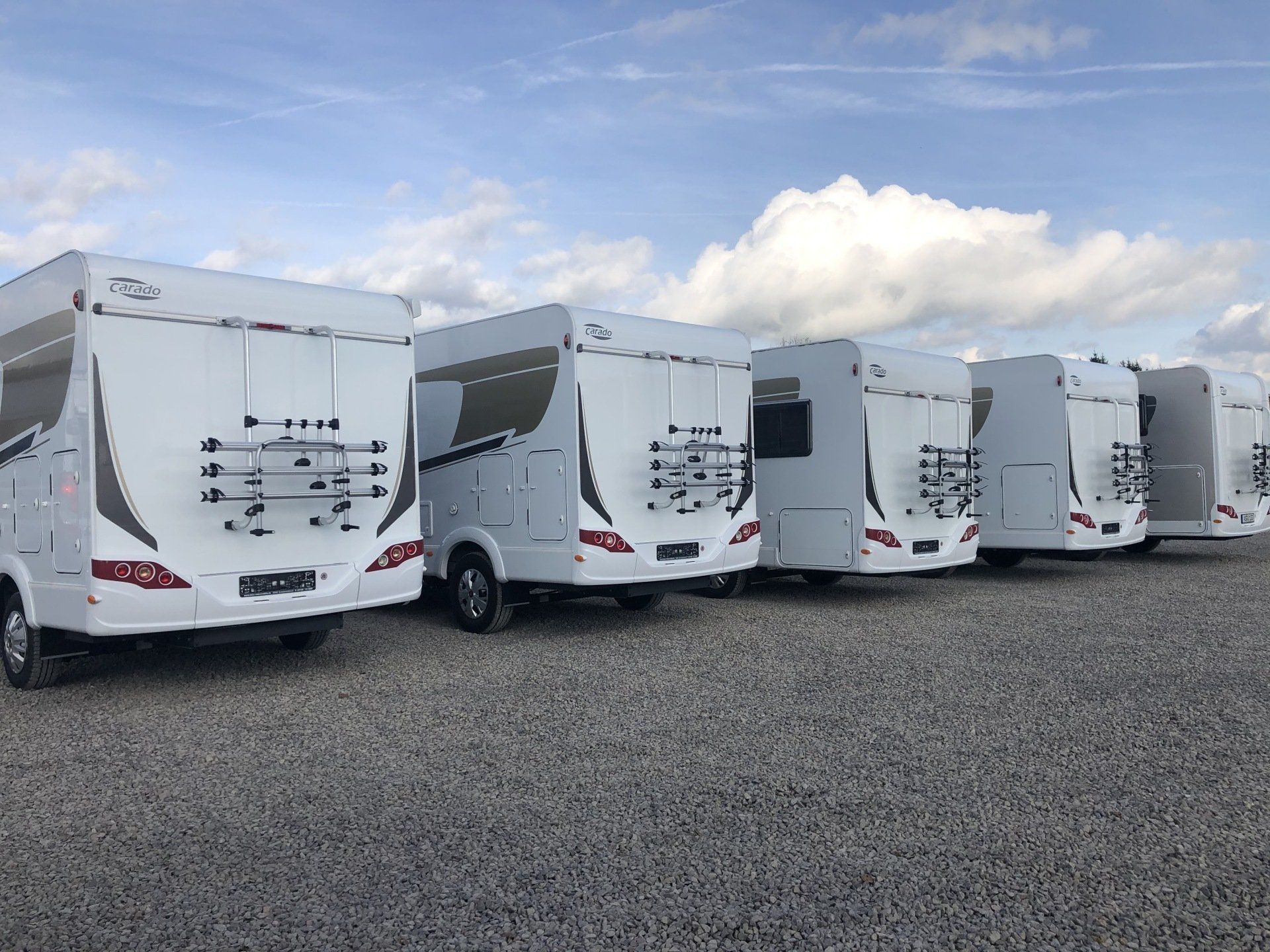 A row of white rvs are parked in a gravel lot.