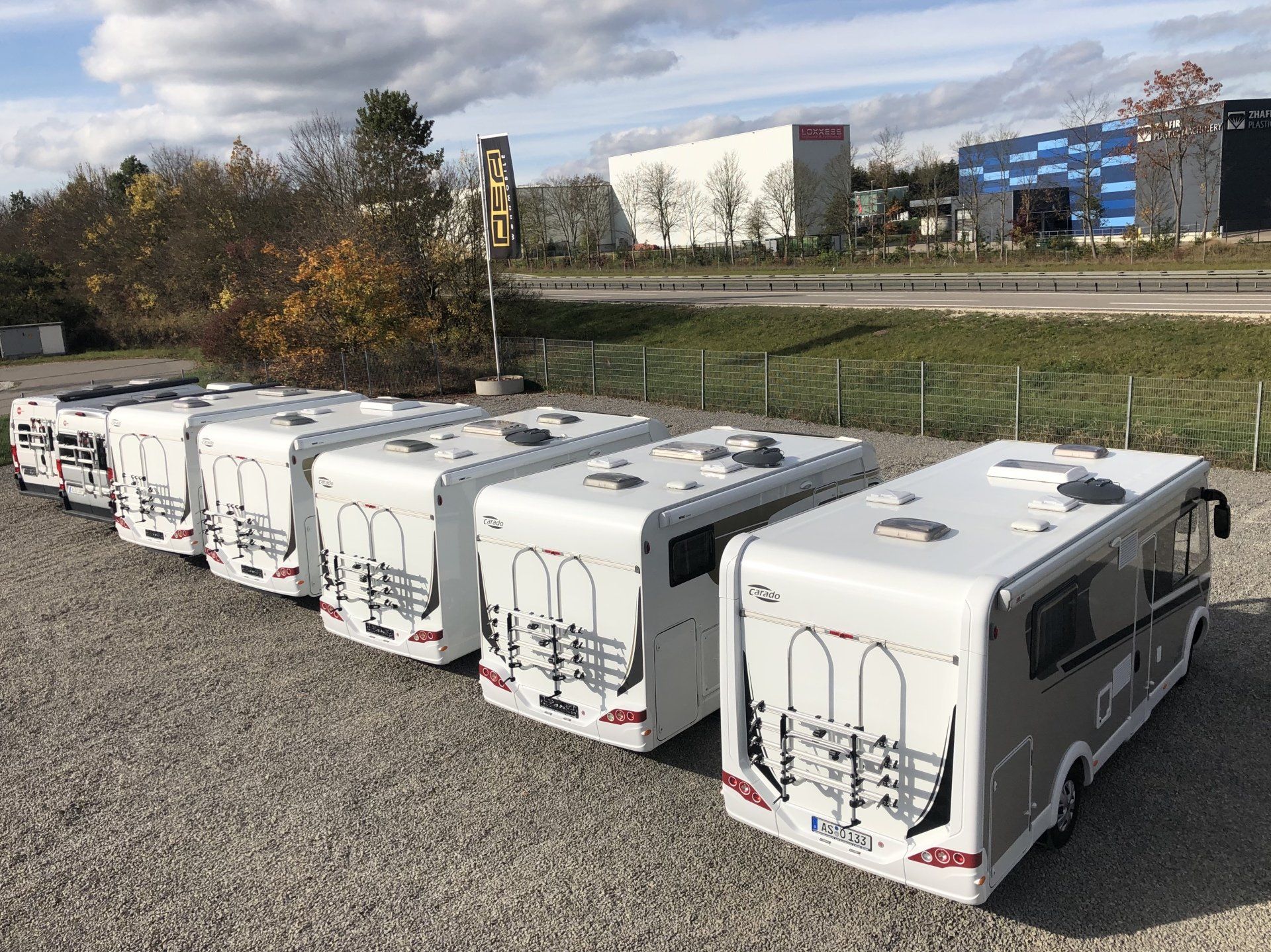 A row of white rvs are parked in a gravel lot.